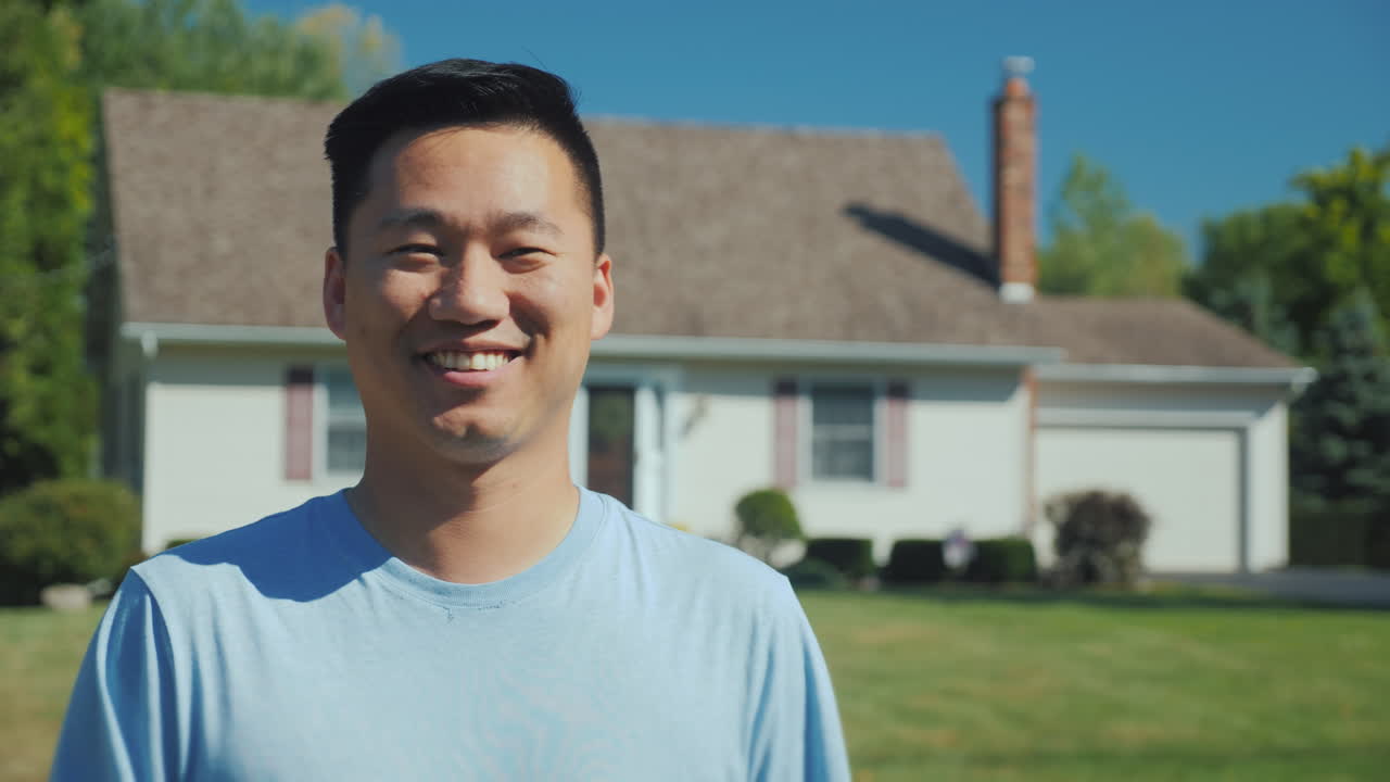 카메라를 보고 웃는 성공을 바라보는 새 집 배경에 있는 행복한 아시아 남자의 초상화