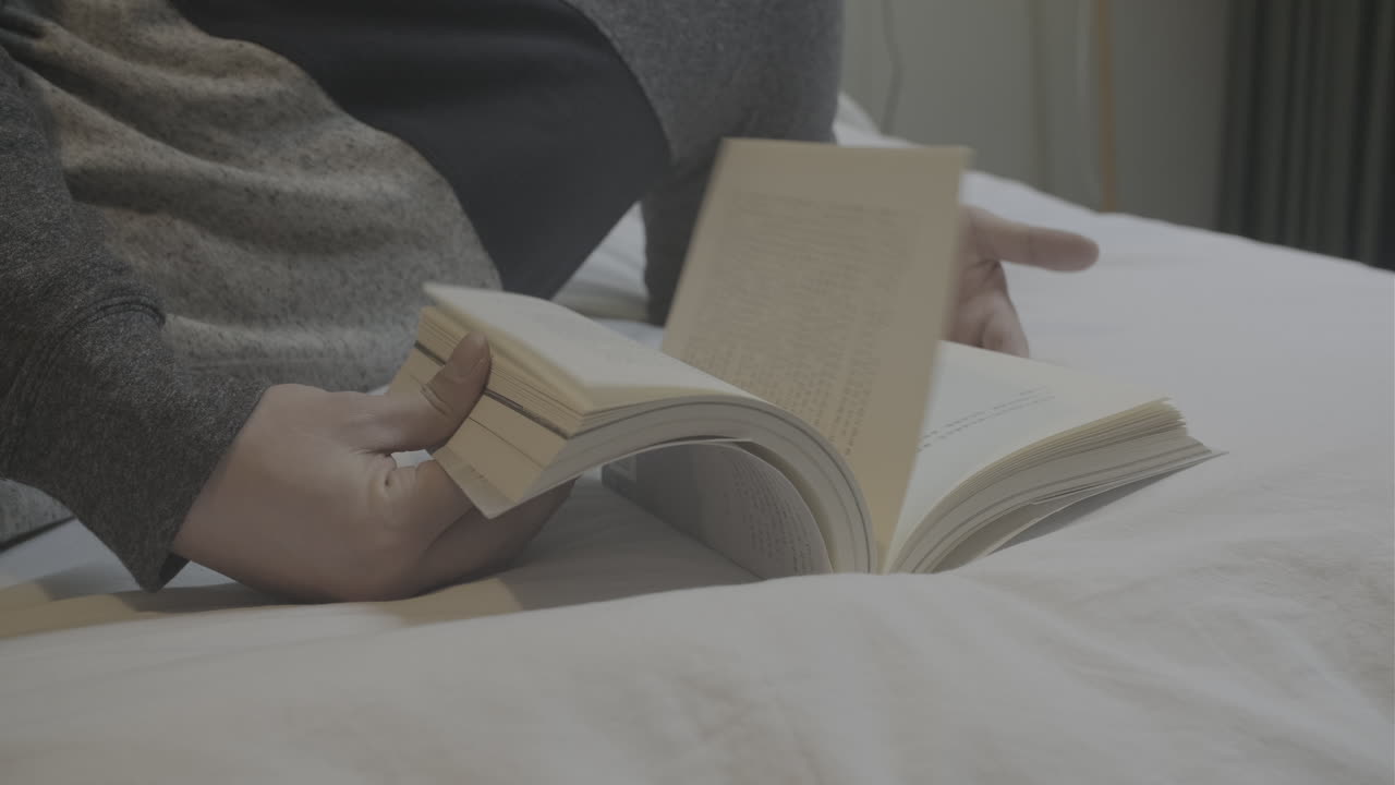 Person turning book pages lying on a bed. Close up shot