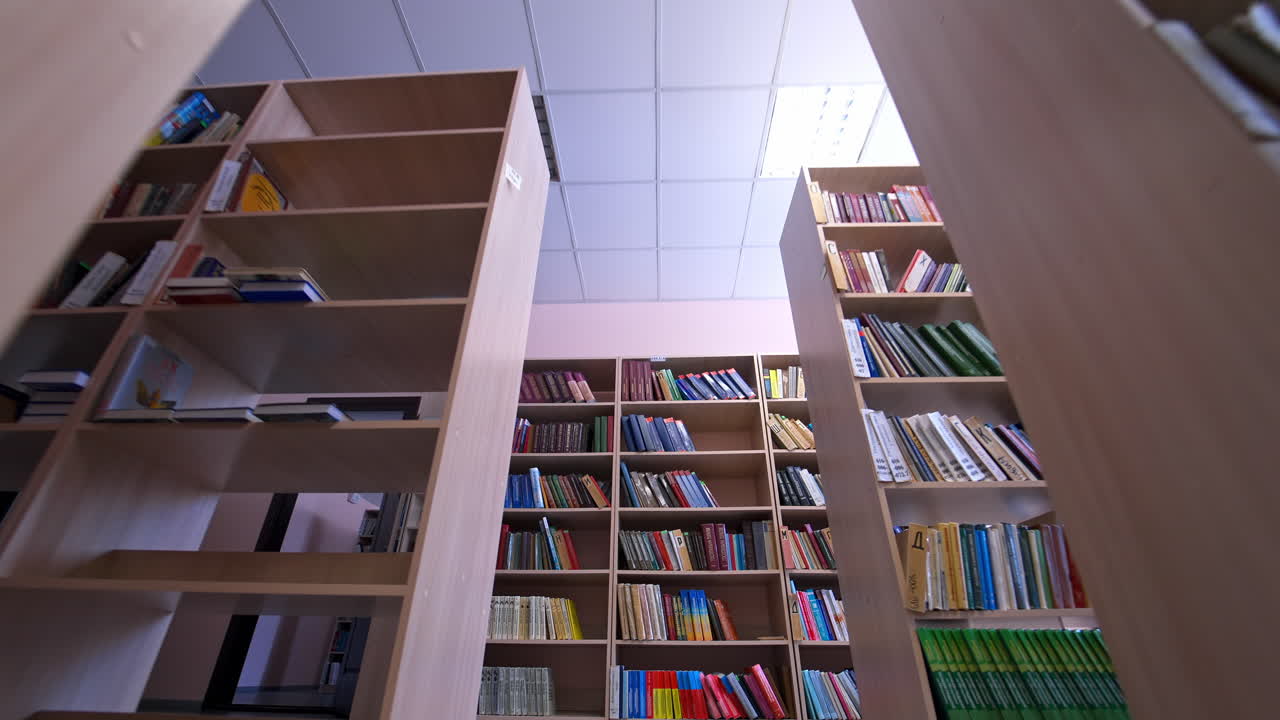 Library books stacked on shelves. Rows of bookcases with books in the library. Education, school or university learning concept. Camera moves back.