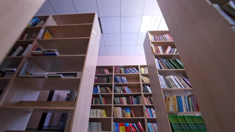 library books stacked on shelves. rows of bookcases with books in the library. education, school or university learning concept. camera moves back.