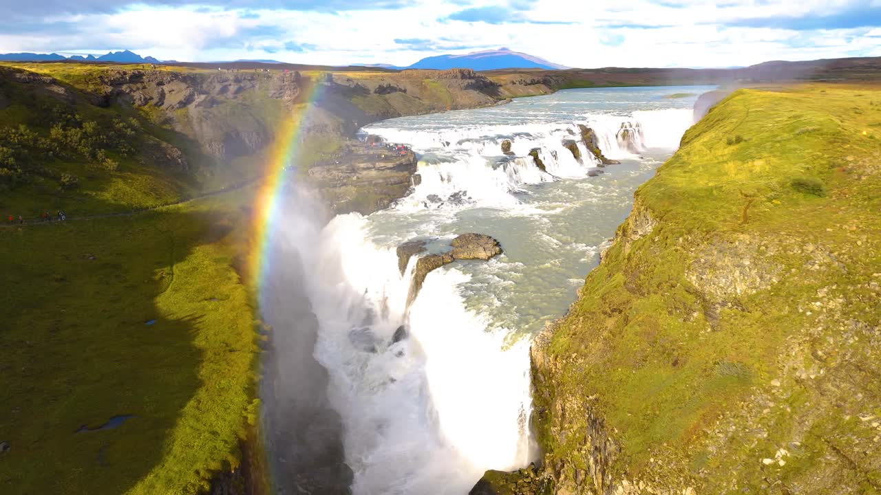 disparo de arco lento de turistas caminando a gullfoss cae con un arco iris vibrante