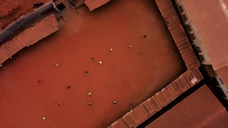 aerial top shot above people playing soccer on red clay in cloudy yaounde, cameroon