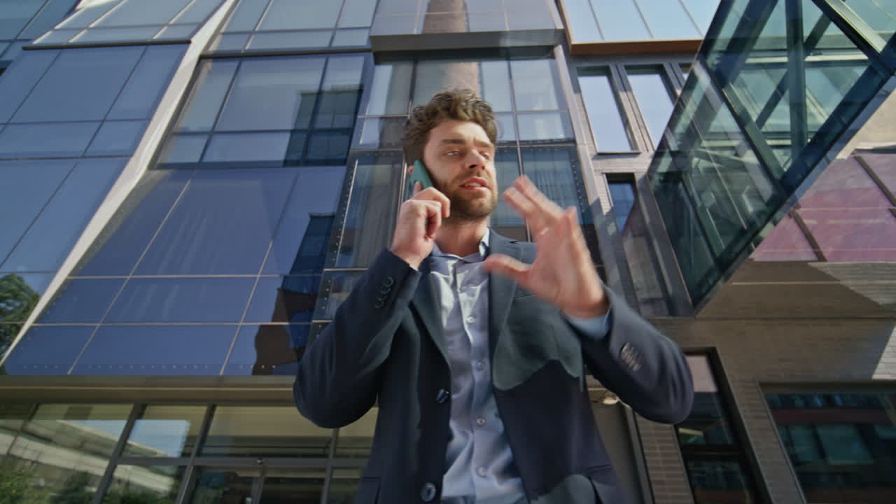 Uomo d'affari stressato che telefona con il cellulare all'esterno di un centro direzionale. Capo irritato.