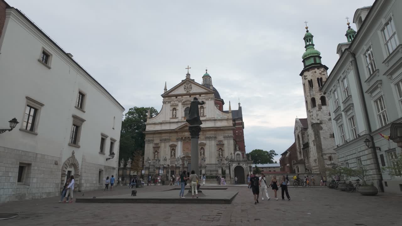Tourists wander through St Mary Magdalene Square in Krakow, Poland, admiring historical architecture against a serene sky. Pan Right Shot