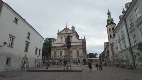 tourists wander through st mary magdalene square in krakow, poland, admiring historical architecture against a serene sky. pan right shot