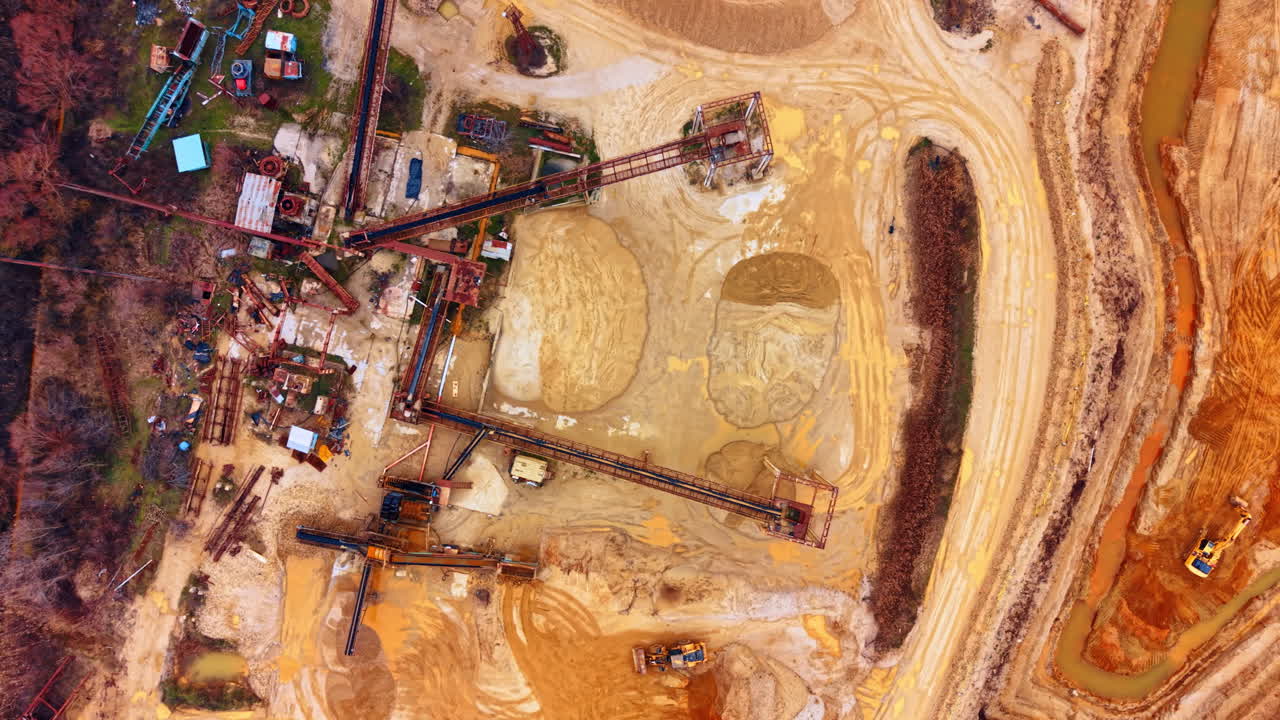 Industrial machinery and conveyor in quarry. Vertical top down shot of quarry infrastructure, conveyor belts, wheel loaders, and tire tracks on sand
