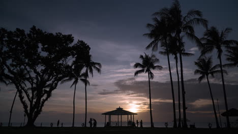 Silhouette-Nicht-Wiederzuerkennender-Menschen-Und-Tropischer-Bäume-Vor-Dem-Atemberaubenden-Sonnenuntergangshimmel-Am-Shangri-La-Resort-Tanjung-Aru-Beach-In-Kota-Kinabalu,-Malaysia