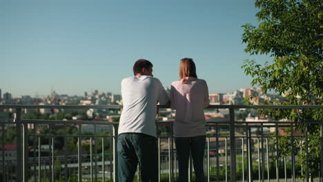 contrapartes de negocios apoyados en una barandilla de hierro participando en una conversación mientras la mujer tiene gafas descansando en la cabeza, el paisaje urbano pintoresco forma un fondo vibrante con vegetación y cielos despejados