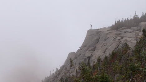 a hiker walks up to and stands on the edge of a cliff in ominous foggy weather in the adirondack mountains of new york