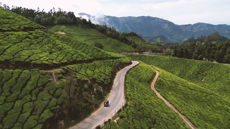 aerial-view-of-a-tuk-tuk-on-the-road-surrounded-by-tea-plantation-in-Munnar,-Kerala---India