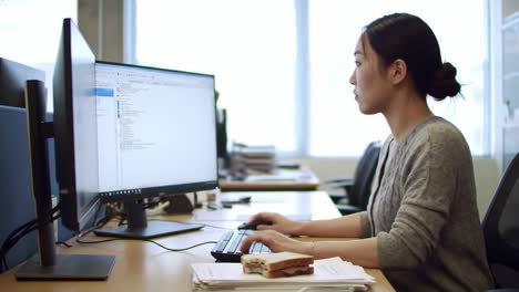 focused professional engaged in office tasks while enjoying a snack, capturing a moment of work-life balance in a busy workplace environment