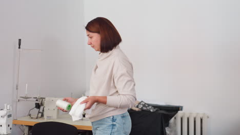dress maker sits beside sewing machine holding fabric from large table, concentrating as she carefully places textile on machine setup, focused on accuracy and alignment in bright workspace