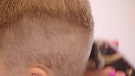 Side-view-of-a-kid-getting-hair-cut-in-a-salon,-Hair-trimmer-movement-close-up-view