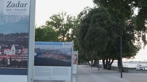 Zadar-promenade-with-info-boards,-walkway-under-shade-of-tree-canopy