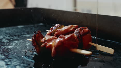 pouring fresh oil onto skewers sitting on festival grill