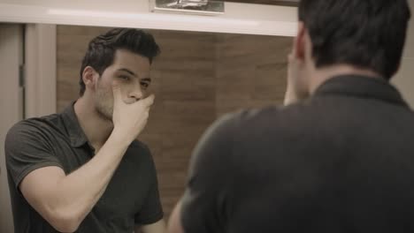 Handsome-man-looking-face-in-front-of-mirror.-Closeup-guy-adjusting-t-shirt
