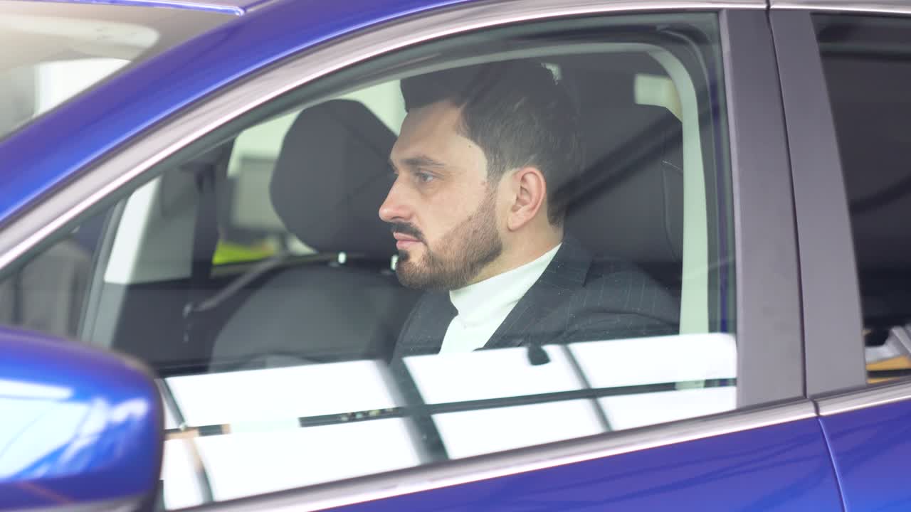 Stylish man sitting in car salon. Young confident guy choosing automobile in showroom