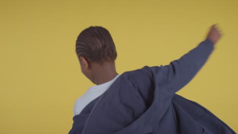 studio portrait of hyperactive boy spinning against yellow background