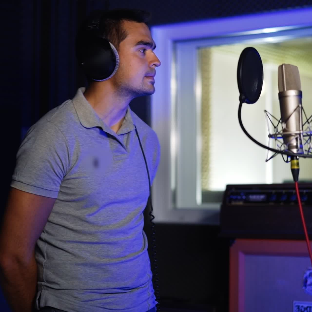 Handsome man wearing headphones on his head stands in the music recording studio. Singer prepared to perform a song and comes up to microphone stand