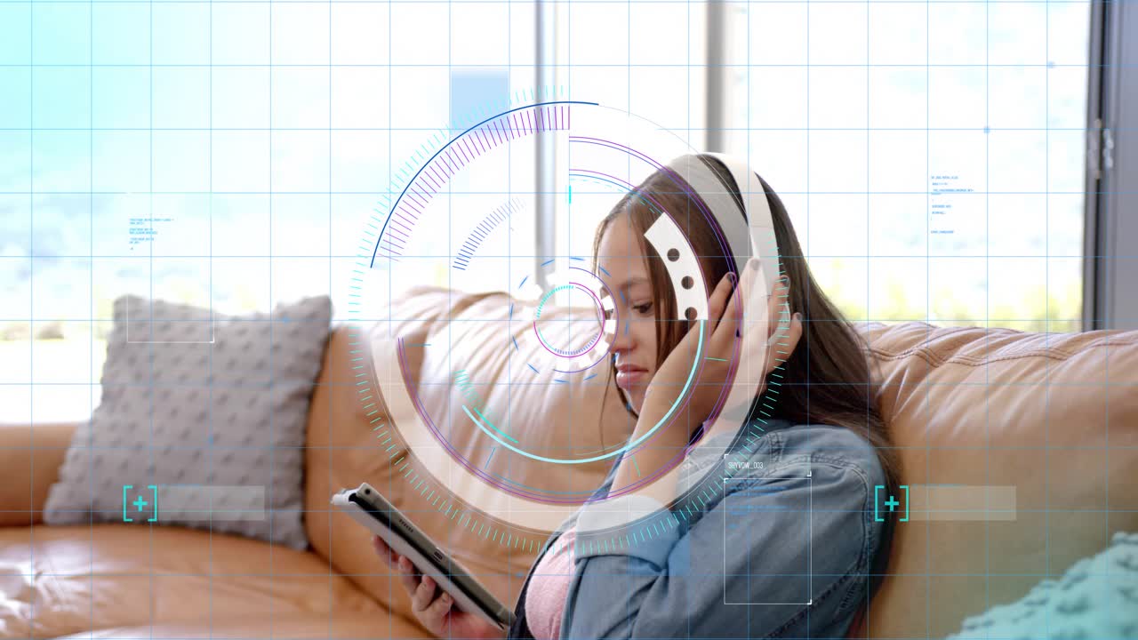 Teenage girl tapping tablet and adjusting headphones on couch, HUD overlay rotating for education