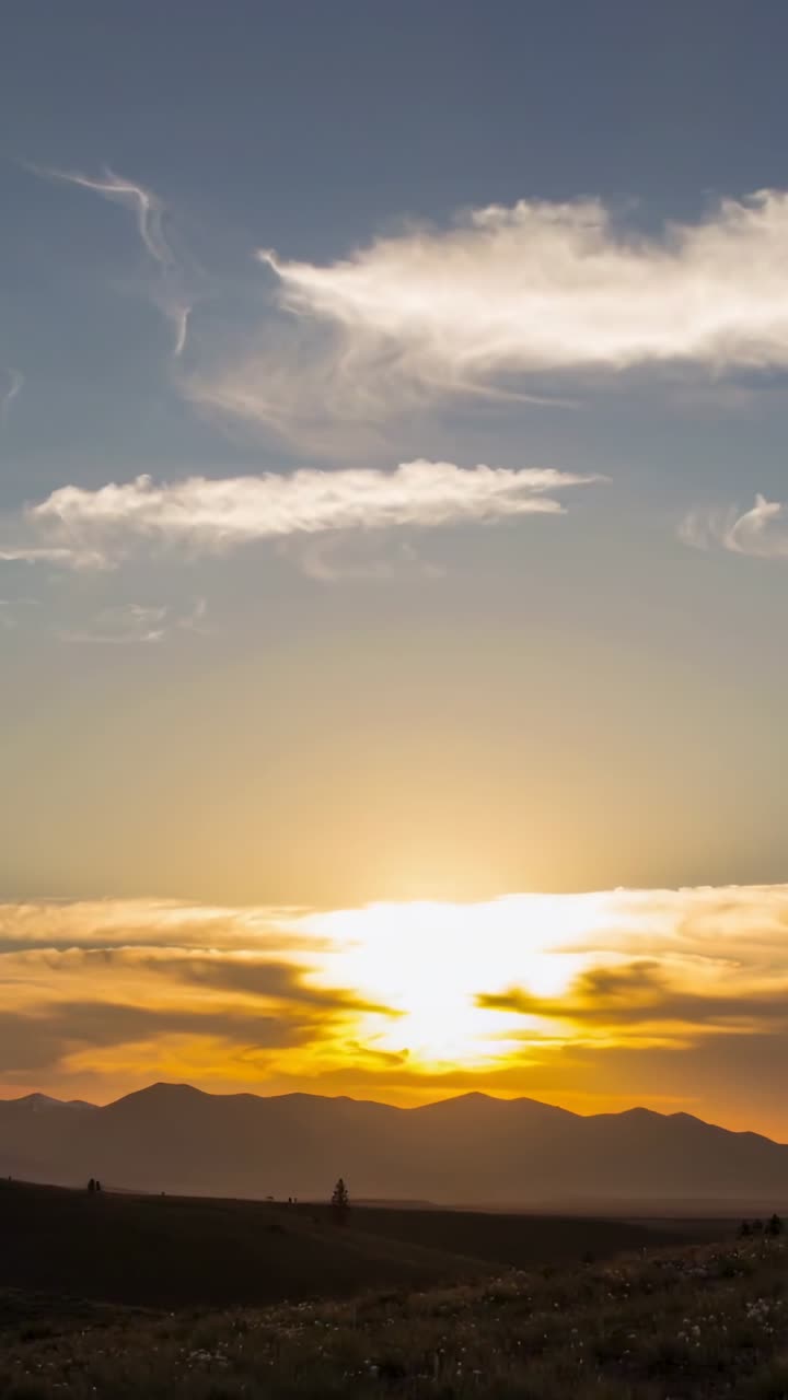 Vertical video: Showing sun sinking behind low cloud at plain, creating glow with range and walkers