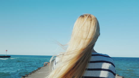 a woman with long hair strolls along the pier the wind ruffles her hair back view