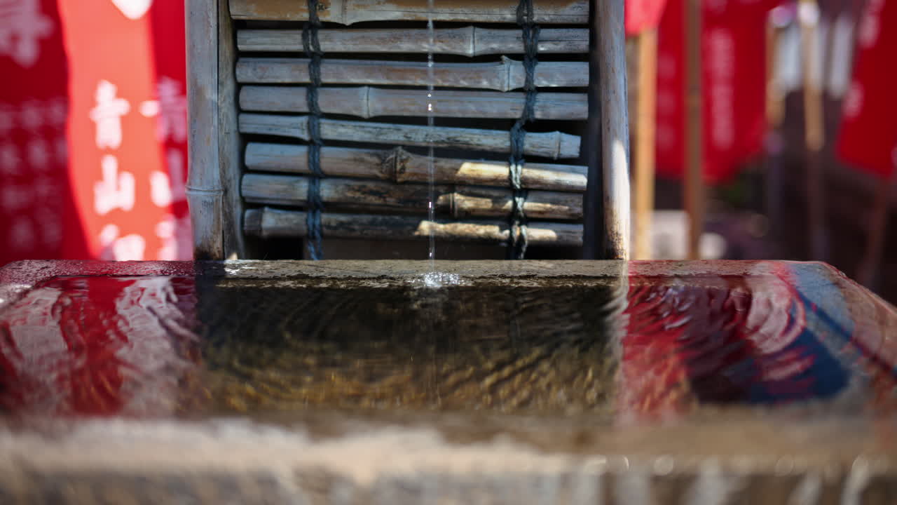 Close up of a small water fountain surrounded by red flags at the Senso-ji temple in Asakusa, Tokyo, Japan