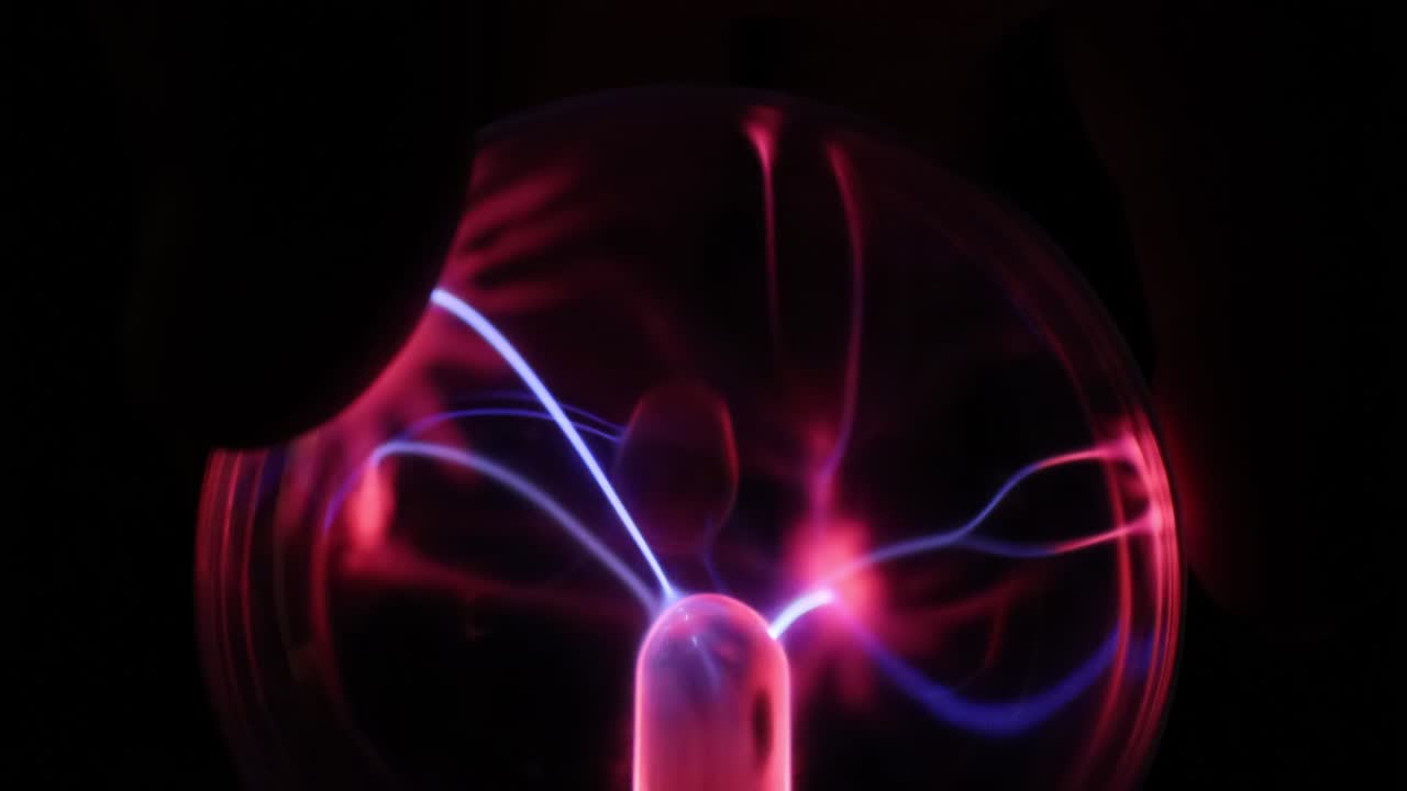 A stunning plasma globe radiates vibrant blue and pink electric arcs from its core, creating a mesmerizing and colorful display of static energy in the dark