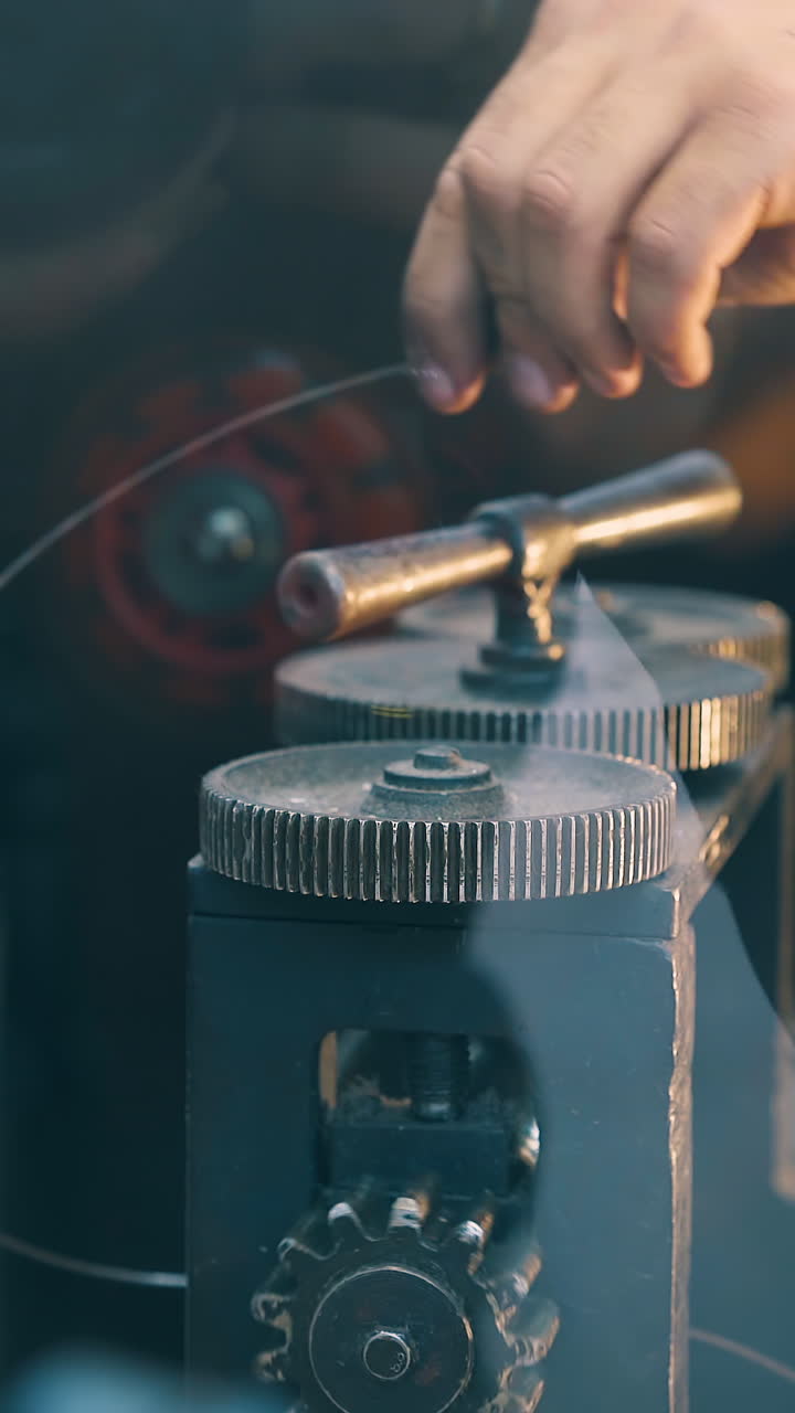 CU: young worker turns handle of modern forge-rolling machine processing long gold rod in jewelry workshop close view