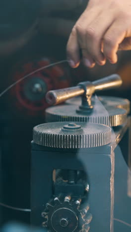cu: young worker turns handle of modern forge-rolling machine processing long gold rod in jewelry workshop close view