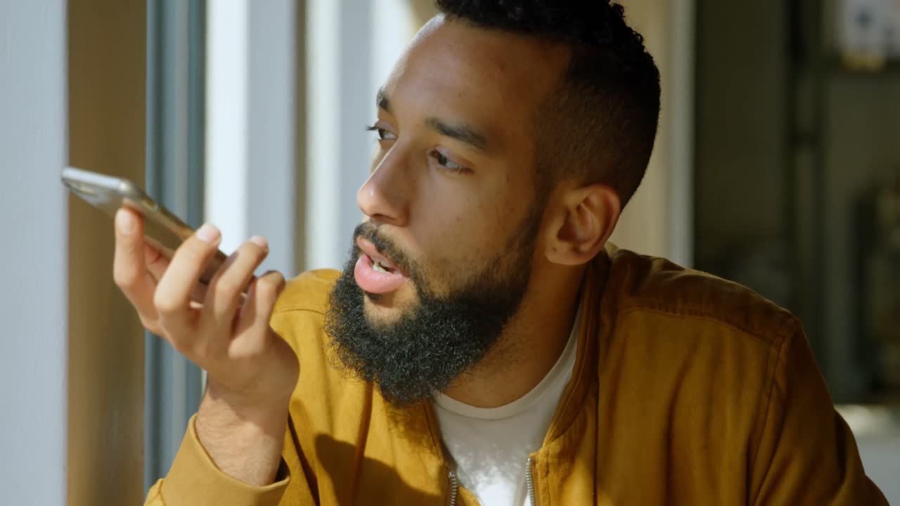 Front view of happy young mixed-race man talking on mobile phone in cafeteria 4k