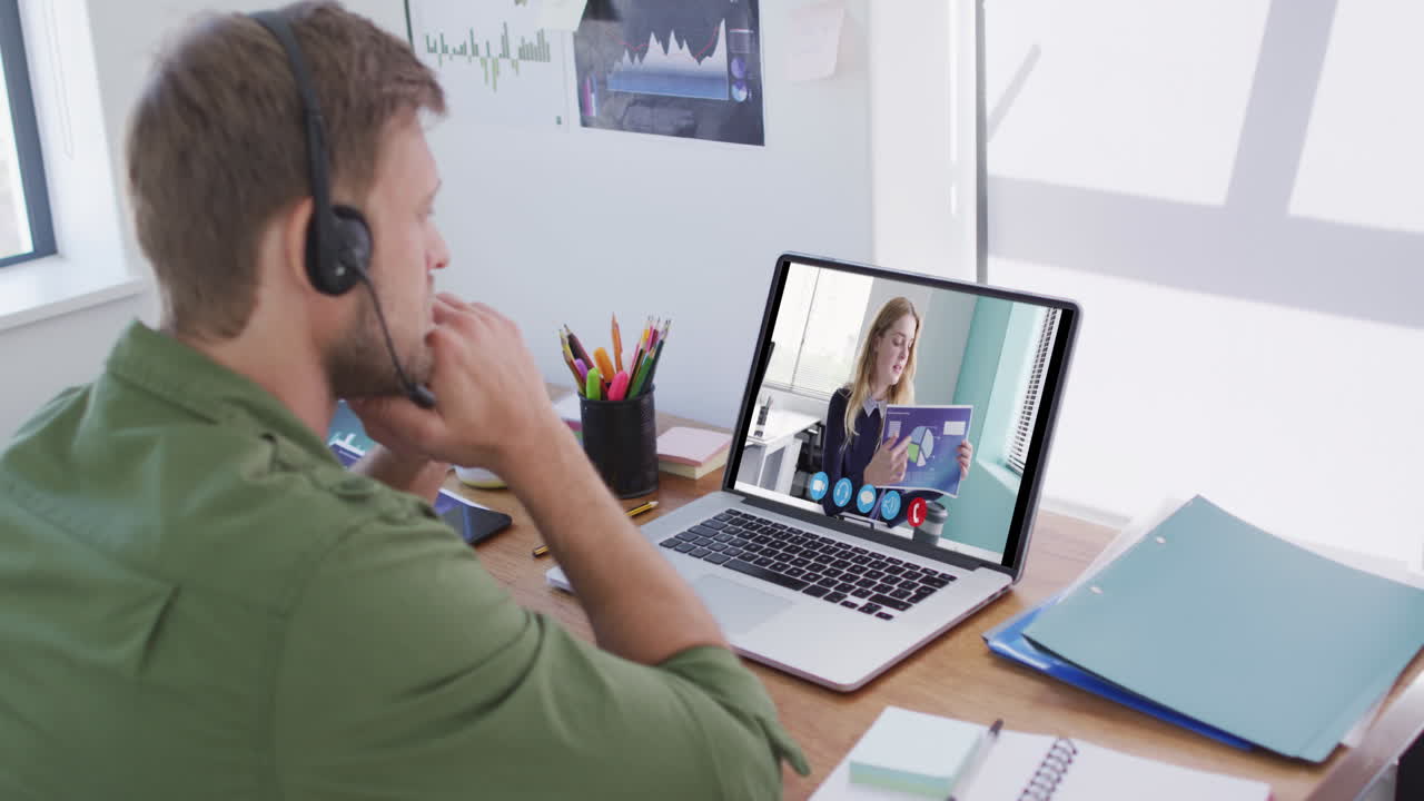 Kaukasisk mand bruger bærbar computer og telefonheadset på videoopkald med en kvindelig kollega.