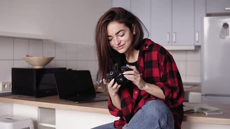atractiva chica morena está tratando de cambiar los ajustes de la cámara mientras está sentada en su cocina en camisa de franela y vaqueros angustiados. cómodo, acogedor apartamento loft.
