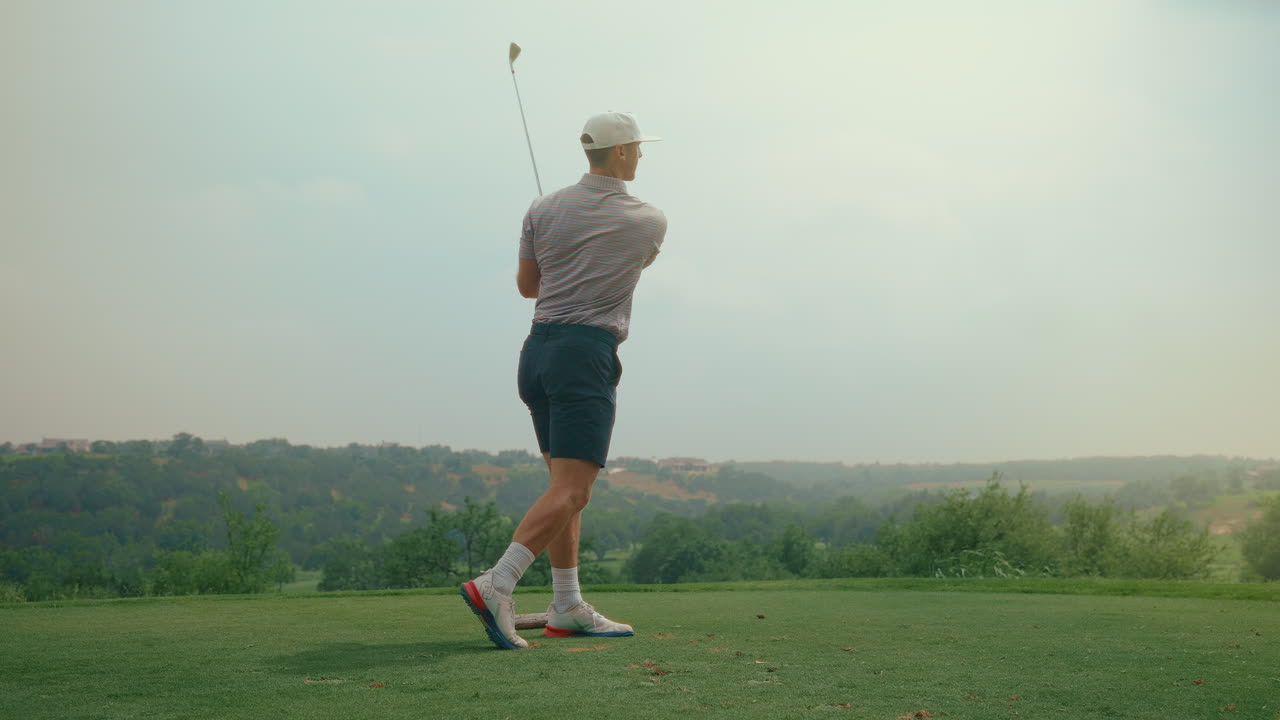 A male golfer hits an iron shot off the tee box in slow motion during golden hour. The warm sunlight highlights the swing’s grace and power on a serene golf course setting.
