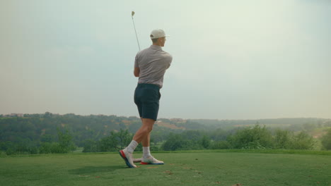 a male golfer hits an iron shot off the tee box in slow motion during golden hour. the warm sunlight highlights the swing’s grace and power on a serene golf course setting.