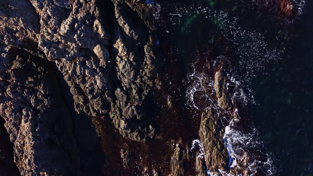Waves crashing against rugged coastal rocks under sunlight create a stunning natural landscape near the ocean