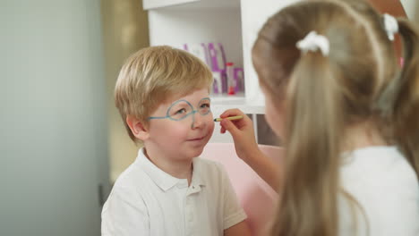 el chico se ríe mientras la chica pinta gafas y líneas alrededor de la nariz.