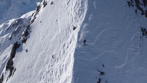 Aerial-orbit-shot-of-professional-skier-resting-on-steep-snowy-slope-in-sunlight