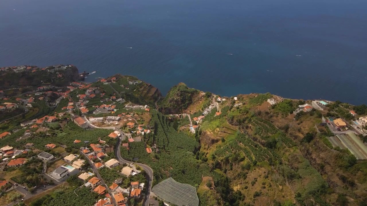 Ampia ripresa drone della campagna di Canhas con sfondo oceanico, che evidenzia l'agricoltura a terrazze unica e il dislivello drammatico dalle pendii montani alla costa atlantica. Drone in movimento in avanti.