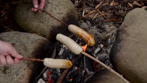 Amigos-Cocinando-Salchichas-En-Palitos-Para-El-Desayuno-Sobre-Una-Fogata-En-Llamas-Al-Aire-Libre