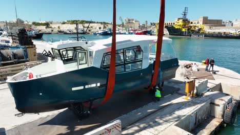 Drohnenaufnahme-Aus-Der-Luft,-Die-Auf-Ein-In-Der-Luft-Gehobenes-Boot-Zufliegt,-Während-Arbeiter-Auf-Der-MMH-Werft-In-Malta-Hebegurte-überprüfen