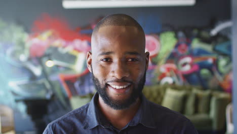 millennial black male creative smiling to camera in front of mural, head and shoulders, close up