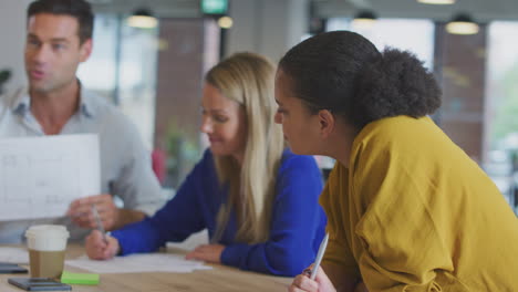 Business-Team-Having-Meeting-Sitting-Around-Table-Discussing-Document-In-Modern-Open-Plan-Office