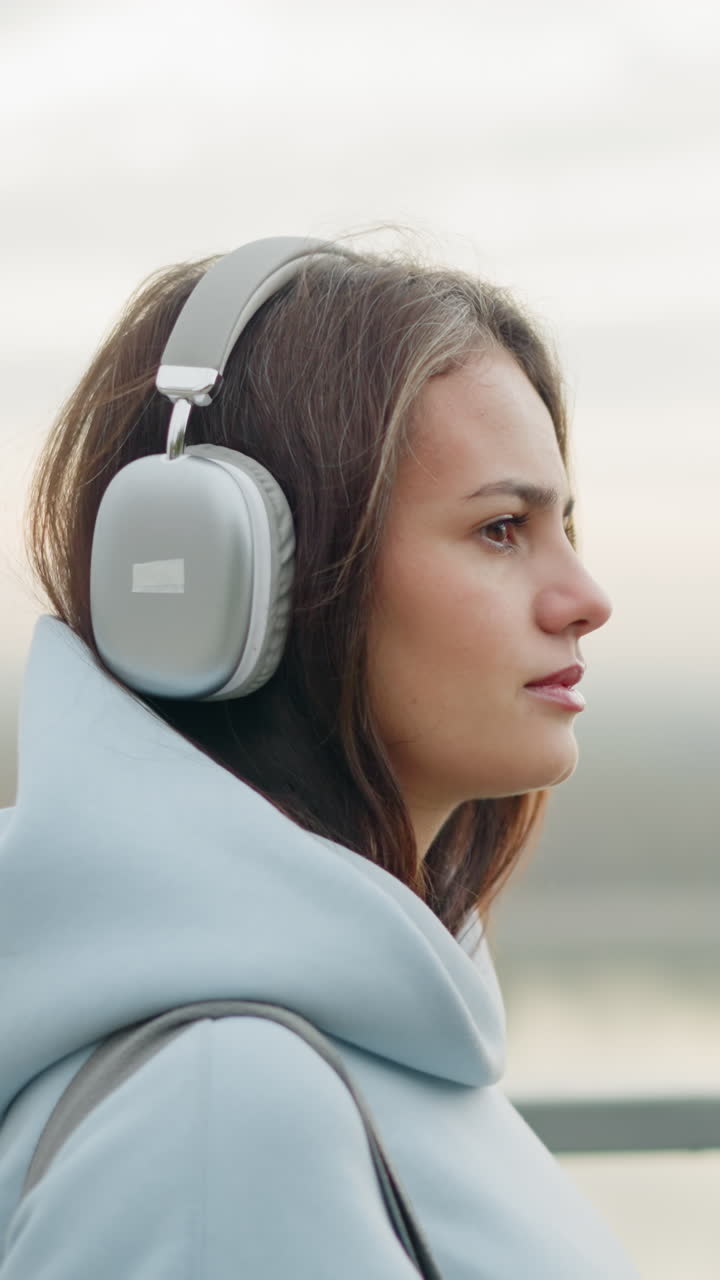 Close-up side view of girl walking majestically, focused and listening to music with headphones, iron rail in background, serene atmosphere, peaceful outdoor stroll in nature, urban setting