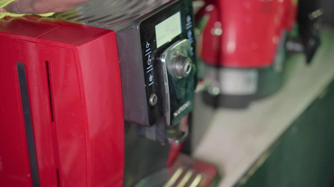 Close-up of red coffee machine with green cloth on top, focusing on cleaning the machine's control panel and surface, showcasing kitchen appliance care and maintenance