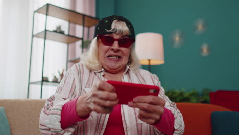 preocupada abuela divertida mujer jugando con entusiasmo a videojuegos de carreras en el teléfono móvil en casa