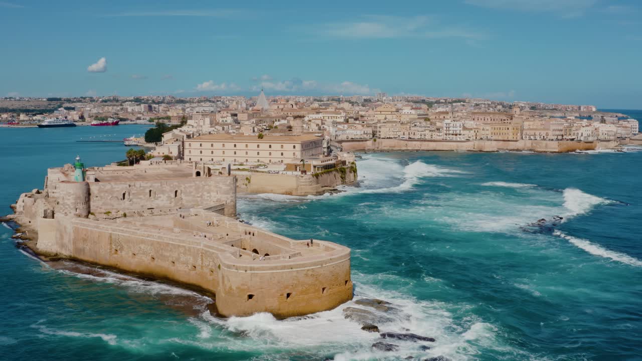 Aerial drone shot of historic castle stretching into the Mediterranean sea in Sicily. Large waves crashing into fortress walls. Castello Maniace in Ortigia island, Syracuse. UNESCO heritage site.
