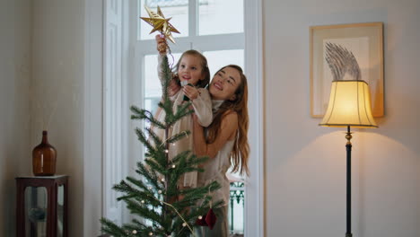 adorable familia preparando la casa de navidad de cerca. niña poniendo el árbol de la estrella de navidad