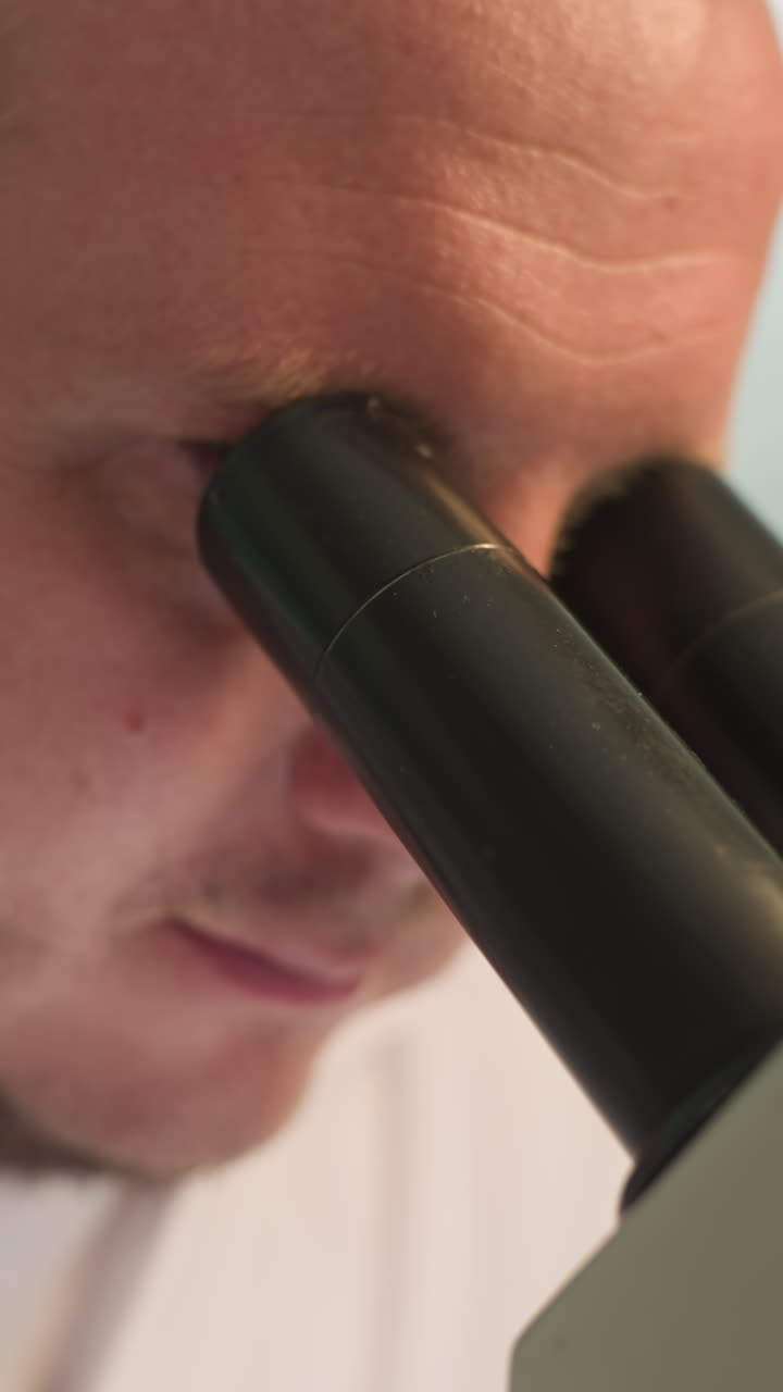 una vista de cerca de un técnico fijó sus ojos en un microscopio en un laboratorio, el primer plano muestra las lentes del microscopio