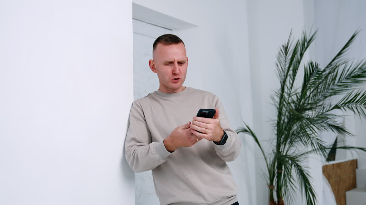 Caucasian male looking at his phone. Man using a gadget standing in the room.